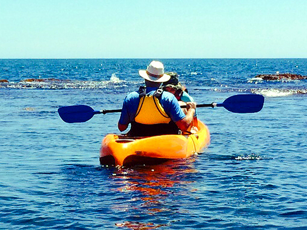 Two people paddling an orange kayak over reef water